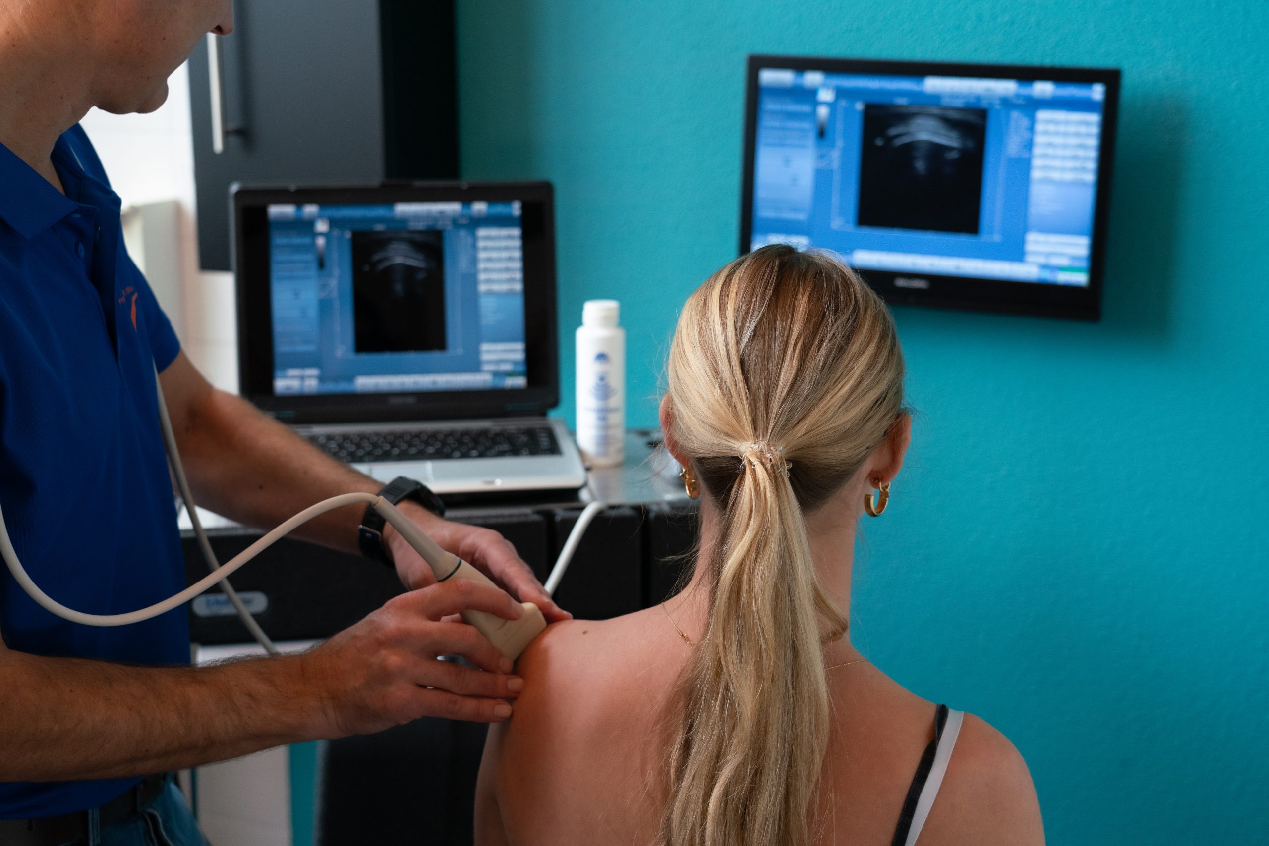 Echografie. De fysiotherapeut gaat met de echoapparatuur over de schouder van de patiënt om er een echo van te maken.